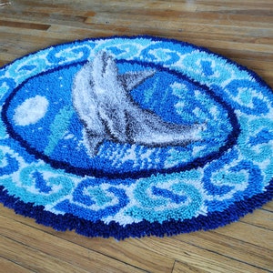 May include: A blue and white rug with a gray dolphin design. The rug has a circular shape and a textured surface.