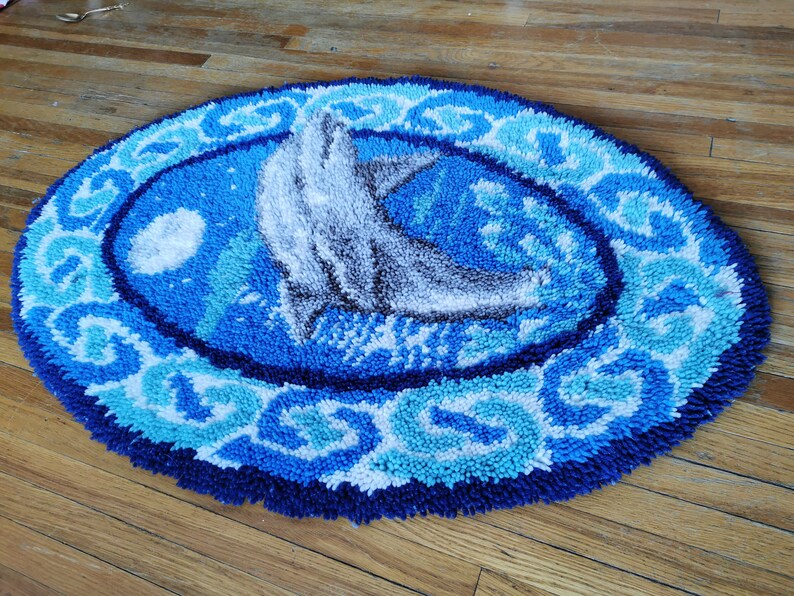 May include: A blue and white rug with a gray dolphin design. The rug has a circular shape and a textured surface.