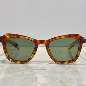 May include: Vintage-style sunglasses with a tortoiseshell pattern frame and green lenses. The frames have a classic, slightly angular shape. The sunglasses are designed for eye protection and fashion.
