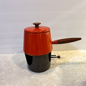 May include: Orange fondue pot with a wooden handle and a black stand. The pot has a lid with a wooden knob.