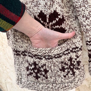 May include: A brown and white knitted cardigan with a geometric pattern. The cardigan has a pocket on the side.