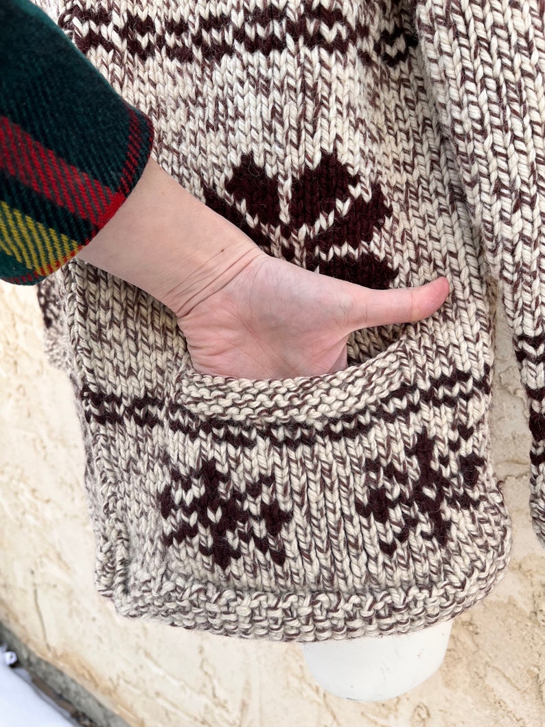 May include: A brown and white knitted cardigan with a geometric pattern. The cardigan has a pocket on the side.