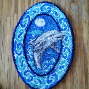 May include: A blue and white oval rug with a dolphin jumping out of the water. The rug has a white border with a blue and white pattern.
