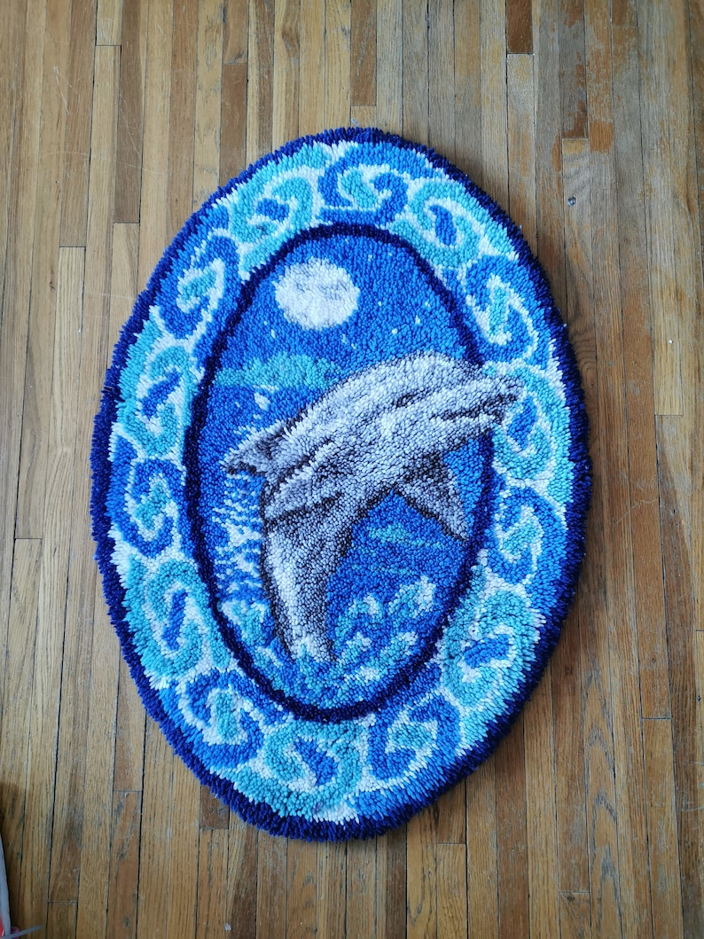 May include: A blue and white oval rug with a dolphin jumping out of the water. The rug has a white border with a blue and white pattern.