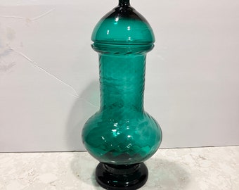 May include: A tall, teal-colored glass jar with a lid. The jar has a bulbous body and a narrow neck. The lid is a dome shape with a small knob on top.