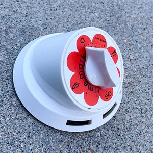 Pode incluir: Temporizador de cozinha branco com um design de flor vermelha. O temporizador tem um dial com números de 0 a 30 e as palavras "turn past" e "remarkable".