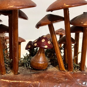 Pu&ograve; includere: Una scultura di funghi in legno con un gruppo di funghi marroni con punti bianchi sui cappelli. I funghi sono disposti in una scena di bosco con muschio e una base in legno.