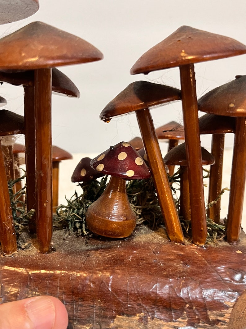 Pu&ograve; includere: Una scultura di funghi in legno con un gruppo di funghi marroni con punti bianchi sui cappelli. I funghi sono disposti in una scena di bosco con muschio e una base in legno.