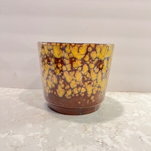 May include: A brown ceramic planter with a yellow and brown speckled glaze.