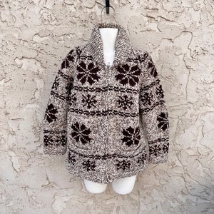 May include: A brown and white knitted cardigan with a zipper closure and a floral pattern. The cardigan has a collar and two pockets.