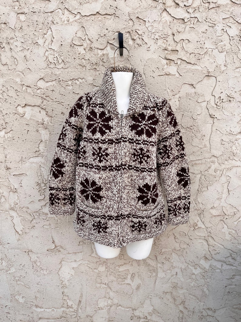 May include: A brown and white knitted cardigan with a zipper closure and a floral pattern. The cardigan has a collar and two pockets.