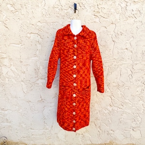 May include: A long orange and brown knitted cardigan with a button-up front and two pockets.