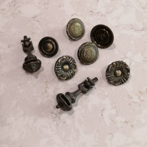 Op de afbeelding: Assortiment van antieke stijl kastknoppen en -grepen in een bronzen afwerking. De knoppen hebben ingewikkelde bloemmotieven en de grepen hebben een eenvoudig, elegant ontwerp.