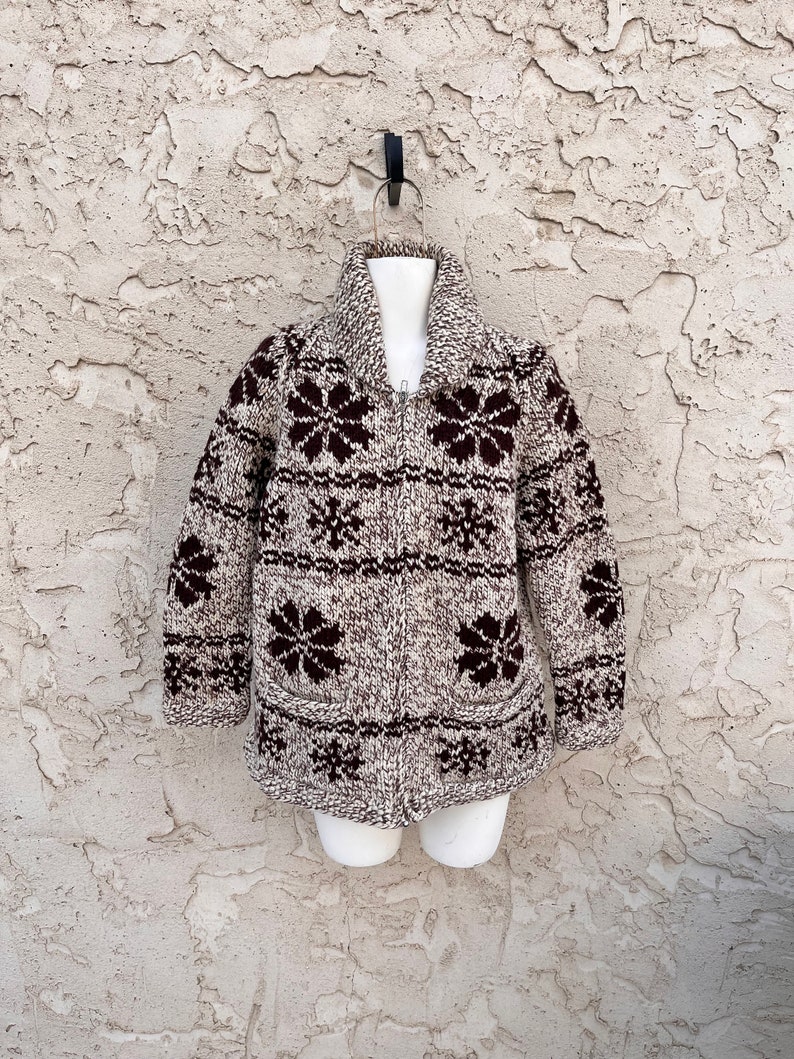 May include: A brown and white knit cardigan with a zipper closure and a snowflake pattern. The cardigan has a brown collar and brown pockets.