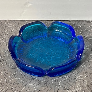 May include: A blue glass ashtray with a textured surface and a rounded, scalloped edge.