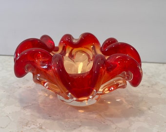 May include: A red and orange glass bowl with a wavy, ruffled edge. The bowl is made of clear glass with a red and orange swirl.