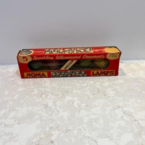May include: A vintage box of Noma Kristal Lamps, containing five sparkling illuminated ornaments. The red box features the product name and the word "indoor". The box is rectangular and has a clear window to view the ornaments.
