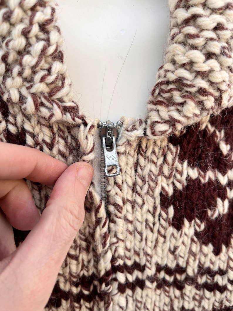 May include: Close-up of a brown and white knitted sweater with a zipper closure. The zipper is silver and has a small metal pull tab.
