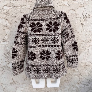 May include: A brown and white knitted sweater with a snowflake pattern. The sweater has a turtleneck and long sleeves.