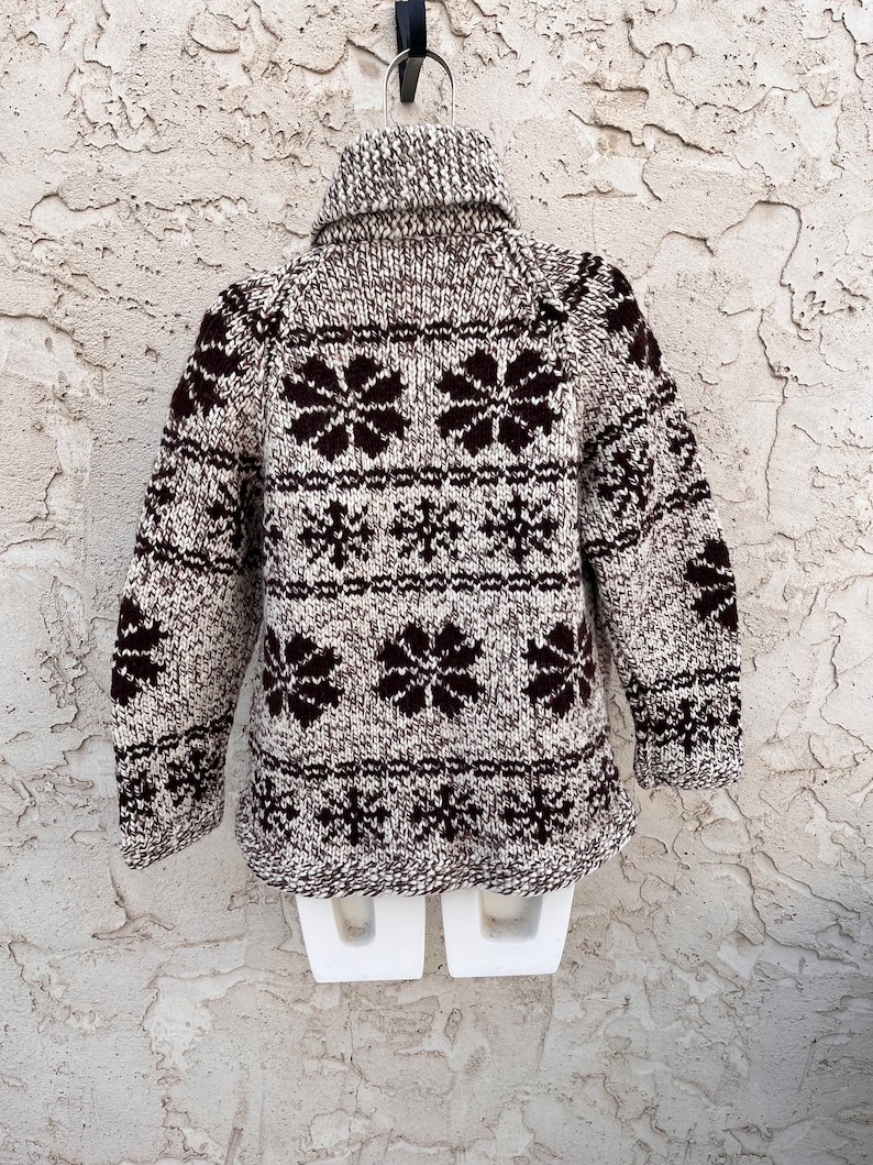 May include: A brown and white knitted sweater with a snowflake pattern. The sweater has a turtleneck and long sleeves.