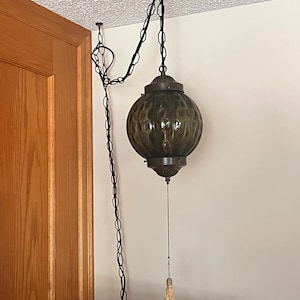 May include: A green glass globe pendant light fixture with a black chain and a tassel pull chain. The light is hanging from the ceiling in a room with a wooden door.