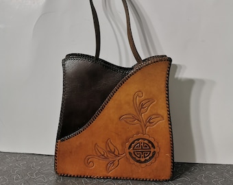 Peut inclure: Un sac cabas en cuir marron avec un motif floral et une bandoulière en cuir marron. Le sac a un bord cousu et un panneau en cuir marron contrastant.