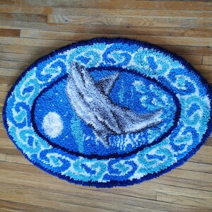 May include: A blue and white oval rug with a white dolphin jumping out of the water. The rug has a blue and white border with a wave pattern.