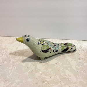 May include: A ceramic bird figurine with a white base and colorful floral designs in shades of blue, green, brown, and yellow.