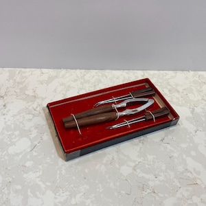 May include: A set of four nutcrackers in a red box. The nutcrackers have wooden handles and silver metal blades.