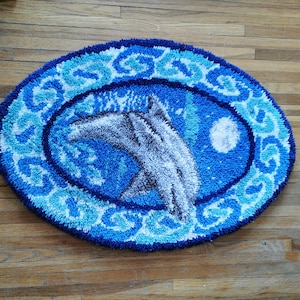 May include: A blue and white oval rug with a white dolphin jumping out of the water. The rug has a blue and white floral design around the edge.