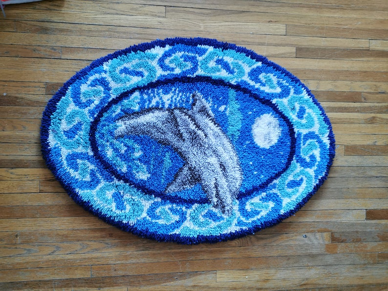 May include: A blue and white oval rug with a white dolphin jumping out of the water. The rug has a blue and white floral design around the edge.