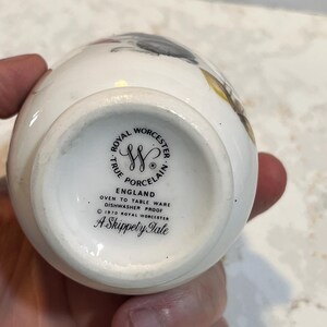 May include: White ceramic egg-shaped vase with a floral design. The bottom of the vase has a black and white logo that reads "Royal Worcester True Porcelain England Oven to Table Ware Dishwasher Proof &copy; 1970 Royal Worcester A Skippety Tale"