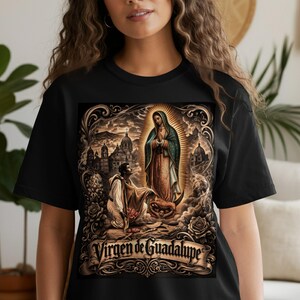 May include: Black t-shirt featuring a detailed graphic of the Virgin of Guadalupe. The image includes a religious scene with figures, architecture, and the text "Virgen de Guadalupe" on a banner. The design is in shades of brown, gold, and cream.