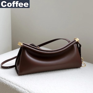 May include: A brown leather handbag with gold-colored hardware. The bag has a curved top handle and a long, adjustable shoulder strap. The word "Coffee" is in a white rectangle in the upper left corner.