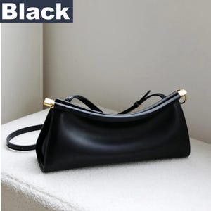 May include: Black handbag with a rectangular shape and a curved top. The bag has a long, adjustable strap and gold-colored accents on the handles. The word "Black" is in a white font in the upper left corner.