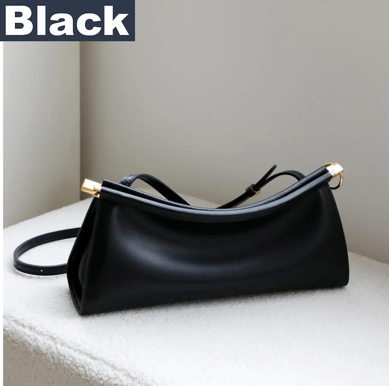 May include: Black handbag with a rectangular shape and a curved top. The bag has a long, adjustable strap and gold-colored accents on the handles. The word "Black" is in a white font in the upper left corner.