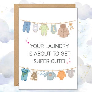 Peut inclure: Carte de vœux à bordure marron avec une illustration de vêtements de bébé sur une corde à linge. Le texte noir dit : « VOTRE LESSIVE VA ÊTRE SUPER MIGNONNE ! ». Le fond est un motif aquarelle de nuages et d'étoiles dorées.