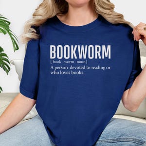 May include: Navy blue t-shirt with the word "BOOKWORM" in large white letters. Below the word is a definition: "A person devoted to reading or who loves books."