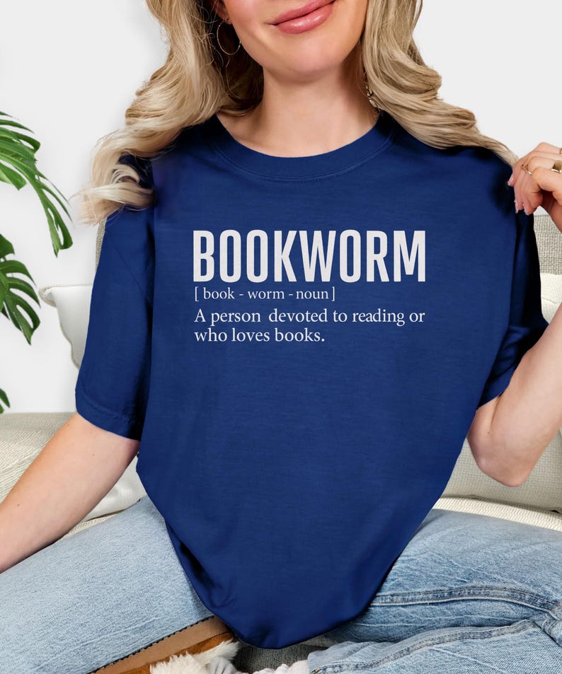 May include: Navy blue t-shirt with the word "BOOKWORM" in large white letters. Below the word is a definition: "A person devoted to reading or who loves books."