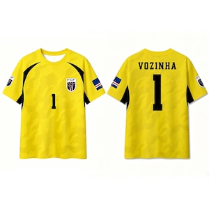 Pode incluir: Uma camisola de futebol amarela de manga curta com um padr&atilde;o de camuflagem tonal subtil, pain&eacute;is laterais pretos e o n&uacute;mero 1 na frente. As costas exibem o nome VOZINHA acima do n&uacute;mero 1 a preto, com pequenas bandeiras nas mangas.