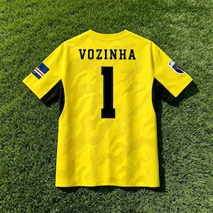 Pode incluir: Uma camisola de futebol de manga curta amarelo brilhante com um padr&atilde;o de chamas tonal subtil. As costas exibem o nome VOZINHA em letras pretas sobre o n&uacute;mero 1. Pequenos emblemas s&atilde;o vis&iacute;veis em ambas as mangas e pain&eacute;is laterais pretos.