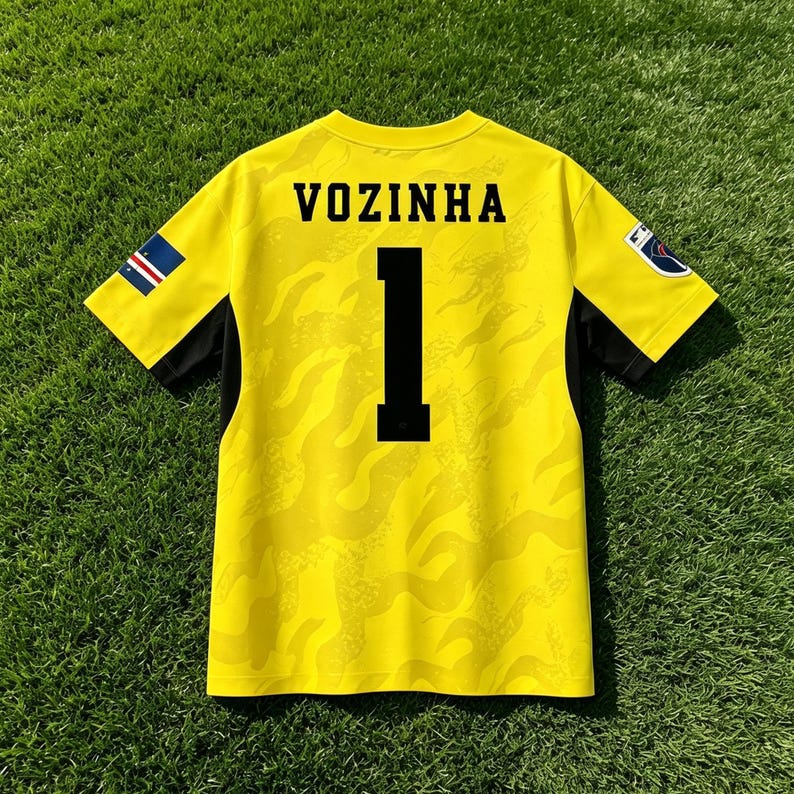 Pode incluir: Uma camisola de futebol de manga curta amarelo brilhante com um padr&atilde;o de chamas tonal subtil. As costas exibem o nome VOZINHA em letras pretas sobre o n&uacute;mero 1. Pequenos emblemas s&atilde;o vis&iacute;veis em ambas as mangas e pain&eacute;is laterais pretos.