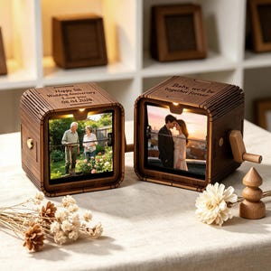 May include: Two dark wood square photo display boxes with hand cranks. The left box is engraved with "Happy 5th Wedding Anniversary. Love you 08.04.2026." and shows a photo of two people in a garden. The right box is engraved with "Baby, we'll be together forever."