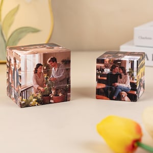 Könnte beinhalten: Zwei personalisierte Foto-Würfel, die jeweils mehrere Bilder zeigen. Ein Würfel zeigt ein Paar mit Pflanzen, der andere ein Paar in einem Café mit einem Hund. Die Würfel stehen auf einer hellen Oberfläche.