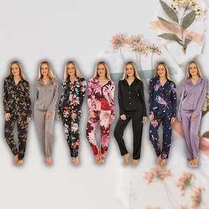 Op de afbeelding: Een collectie damespyjamasets in diverse kleuren en bloempatronen. De sets bevatten shirts met lange mouwen en knopen en bijpassende broeken. Kleuren variëren van zwart met gouden bloemen tot effen zwart, paars en grijs.