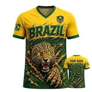 Puede incluir: Una camiseta de cuello en V amarilla y verde con la palabra BRAZIL en letras verde oscuro, un gráfico de un jaguar rugiendo y la bandera de Brasil en la manga. La parte trasera muestra el texto YOUR NAME sobre el número 10 en verde oscuro.