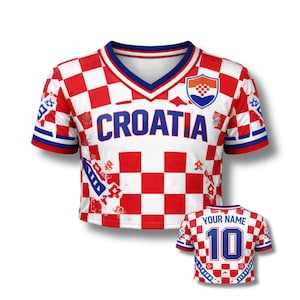 May include: A cropped white and red checkered Croatia soccer jersey with the word "CROATIA" in blue. The jersey has a blue and white V-neck collar and blue sleeve trim. A smaller jersey with "YOUR NAME" and the number 10 is also shown.