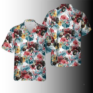 Puede incluir: Una camisa de manga corta con un estampado repetido de tractores rojos, flores tropicales y hojas verdes sobre un fondo blanco. La camisa tiene cuello en V y un corte relajado, adecuada para ropa casual.