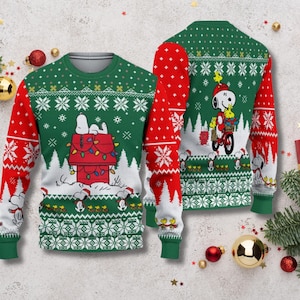 Könnte beinhalten: Ein grüner und roter Weihnachtspullover mit Snoopy und seinem Hundehütte. Die Vorderseite des Pullovers zeigt Snoopy, der auf seinem mit Weihnachtsbeleuchtung geschmückten Hundehütte schläft. Die Rückseite zeigt Snoopy auf einem Fahrrad. Die Ärmel sind rot mit weißen Schneeflockenmustern.