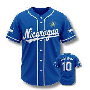 May include: A royal blue baseball jersey with white accents, featuring the word "Nicaragua" in white script across the chest. The jersey includes the Nicaraguan flag on the sleeve and a small emblem. A smaller jersey with "YOUR NAME" and the number "10" is also visible.